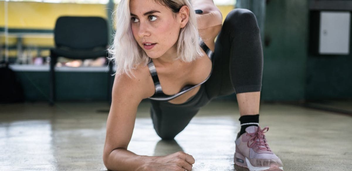 Focused woman with blond hair stretching indoors, showcasing determination and fitness.