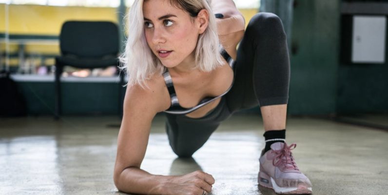 Focused woman with blond hair stretching indoors, showcasing determination and fitness.
