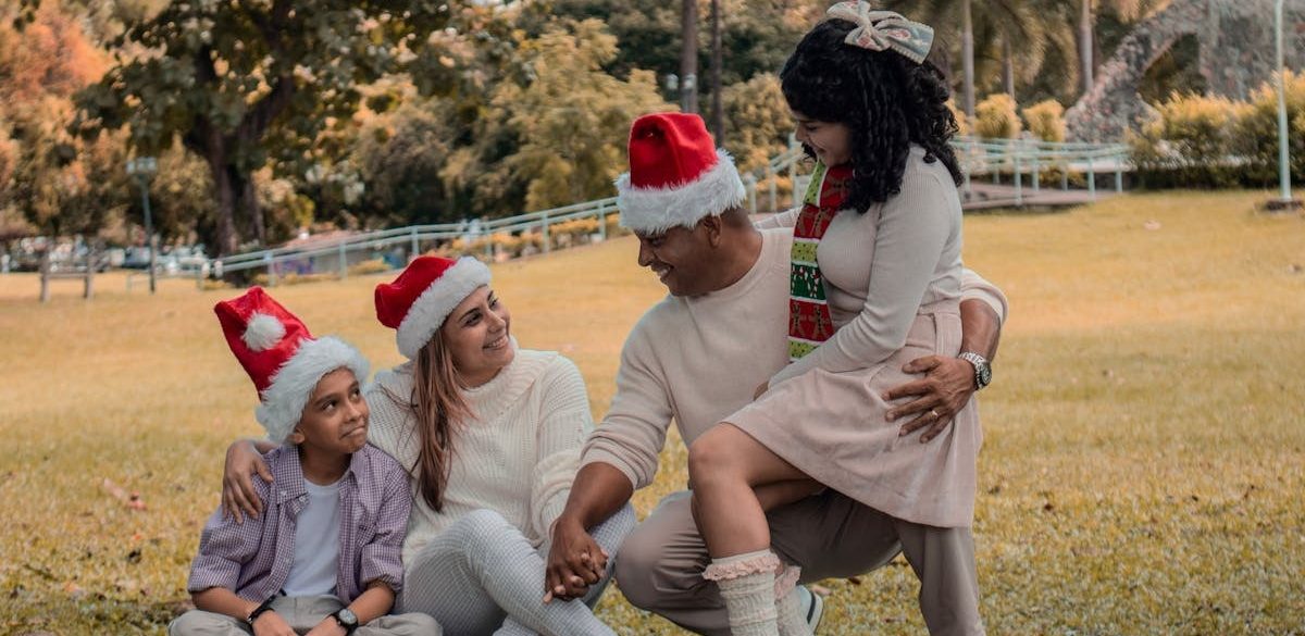 A joyful family wearing Santa hats enjoying Christmas in a sunny park.