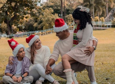 A joyful family wearing Santa hats enjoying Christmas in a sunny park.
