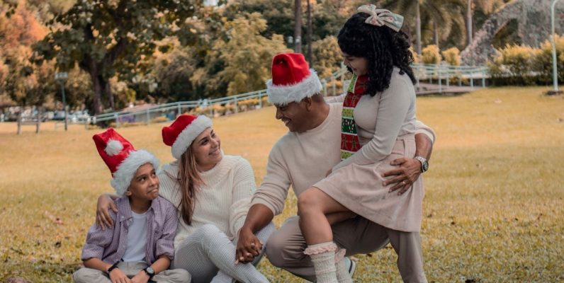 A joyful family wearing Santa hats enjoying Christmas in a sunny park.