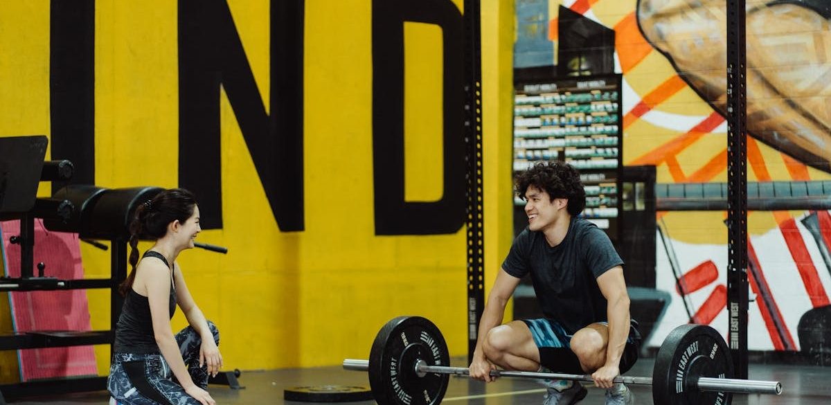 Two young adults in a gym participating in a weightlifting session, sharing a positive moment.
