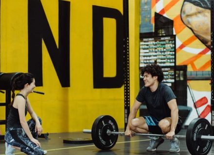 Two young adults in a gym participating in a weightlifting session, sharing a positive moment.