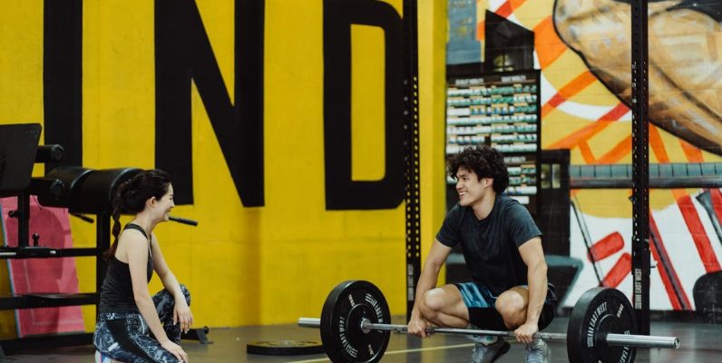 Two young adults in a gym participating in a weightlifting session, sharing a positive moment.