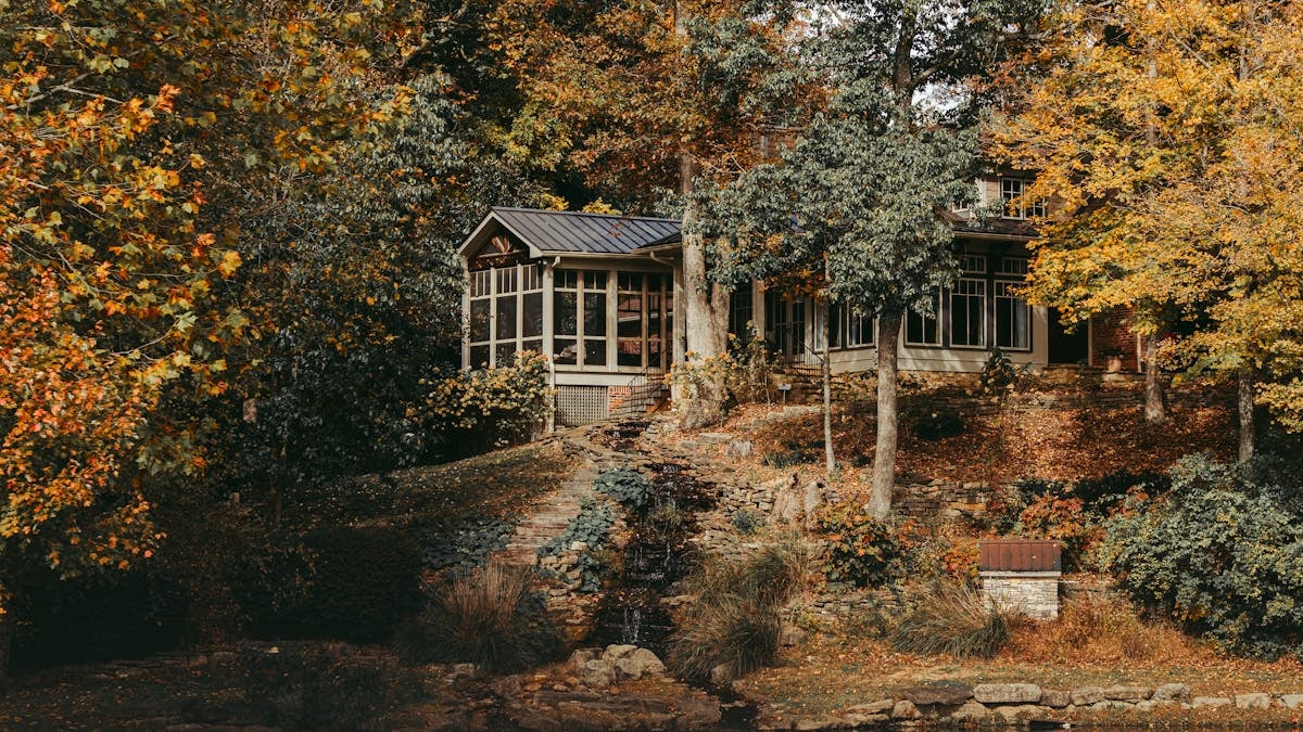 Beautiful fall scene of a cozy cottage surrounded by colorful autumn trees by a tranquil lake.